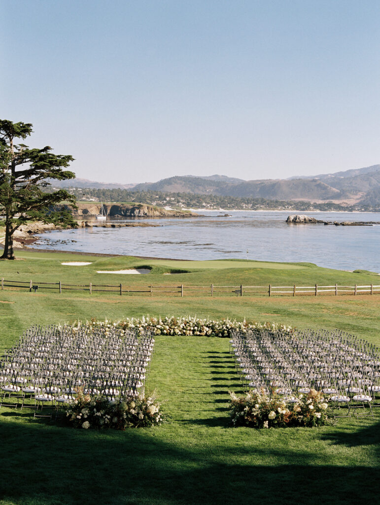 wedding Ceremony space set up with chairs on green grass and flowers overlooking the ocean
