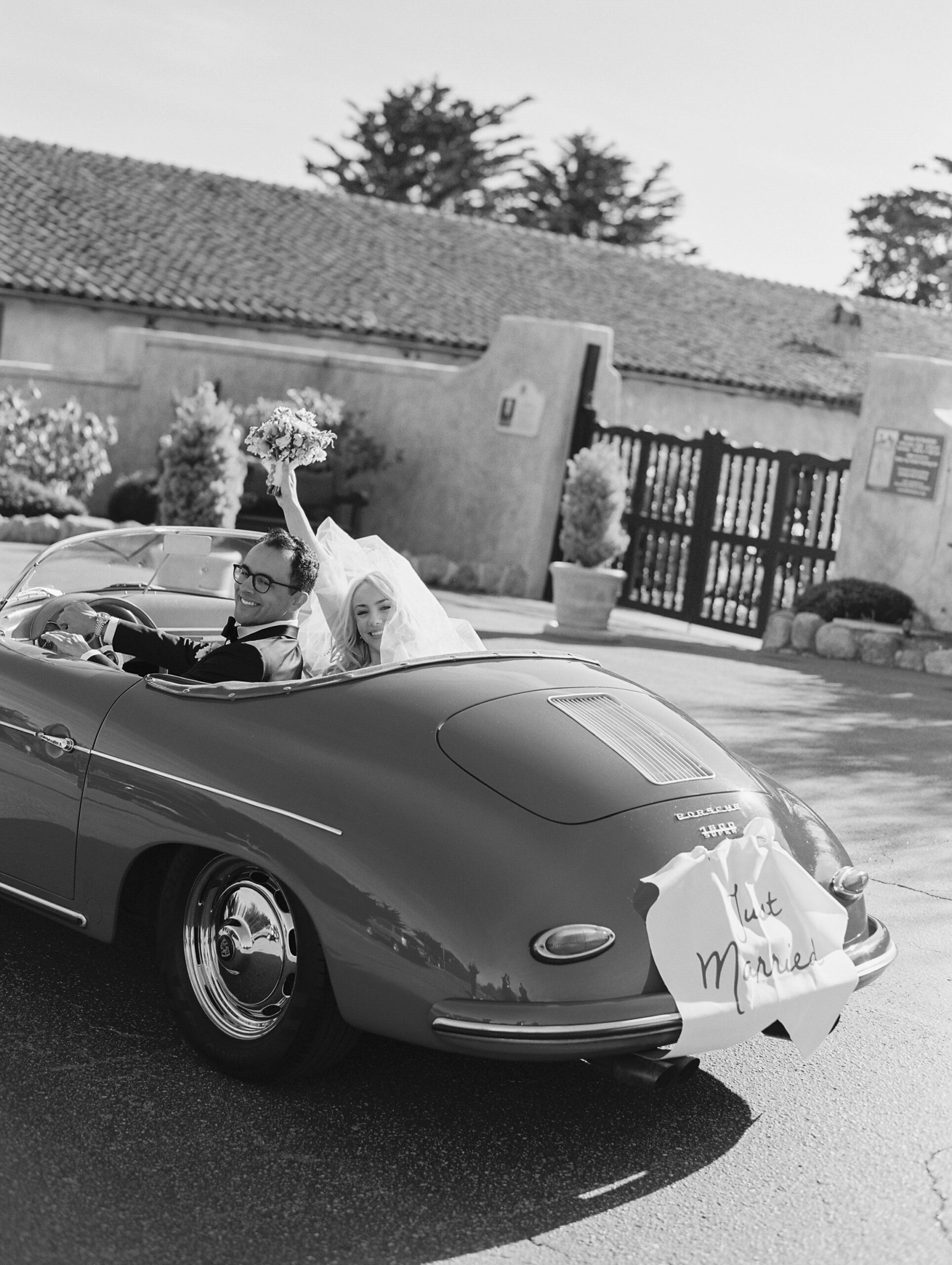 couple in red Porsche with just married sign on the back leaving the Carmel mission church in the background. 