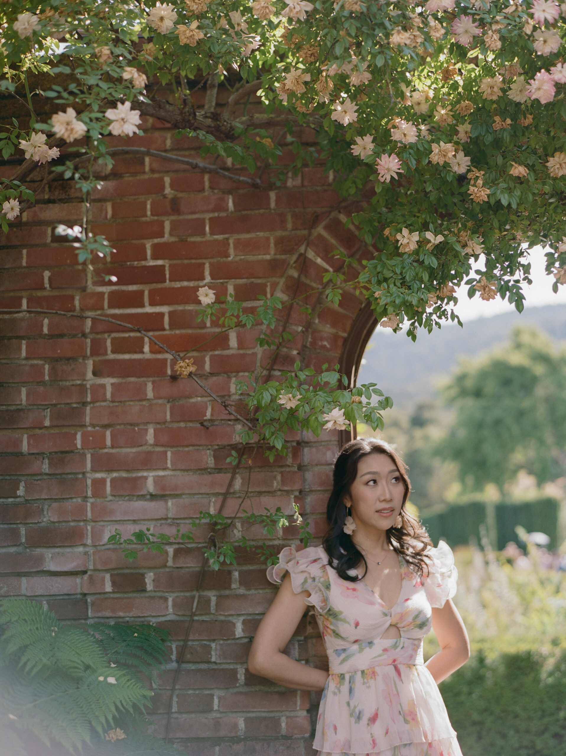 girl leaning back on a brick wall with pink floral vines on top of the wall