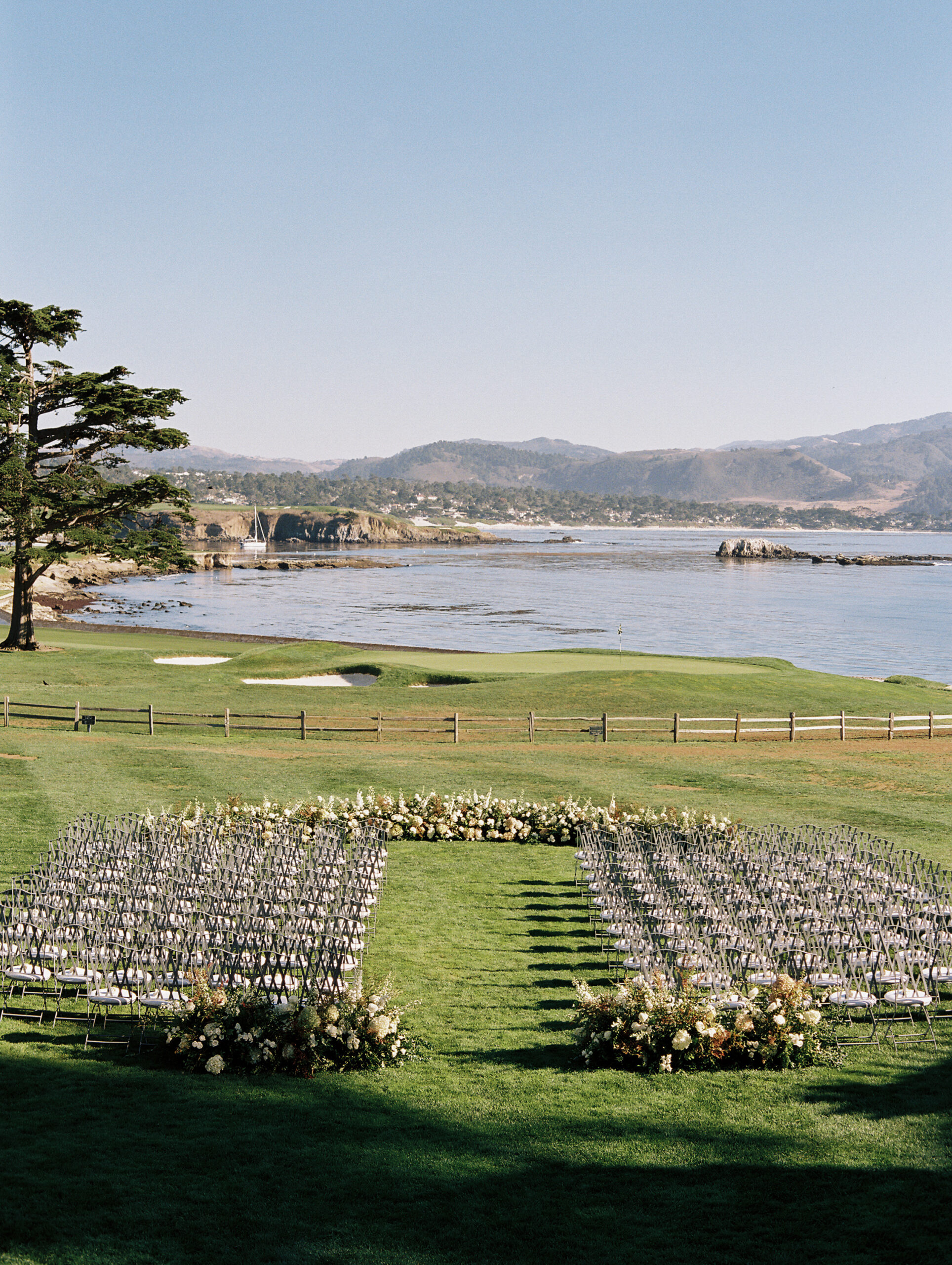 wedding Ceremony space set up with chairs on green grass and flowers overlooking the ocean