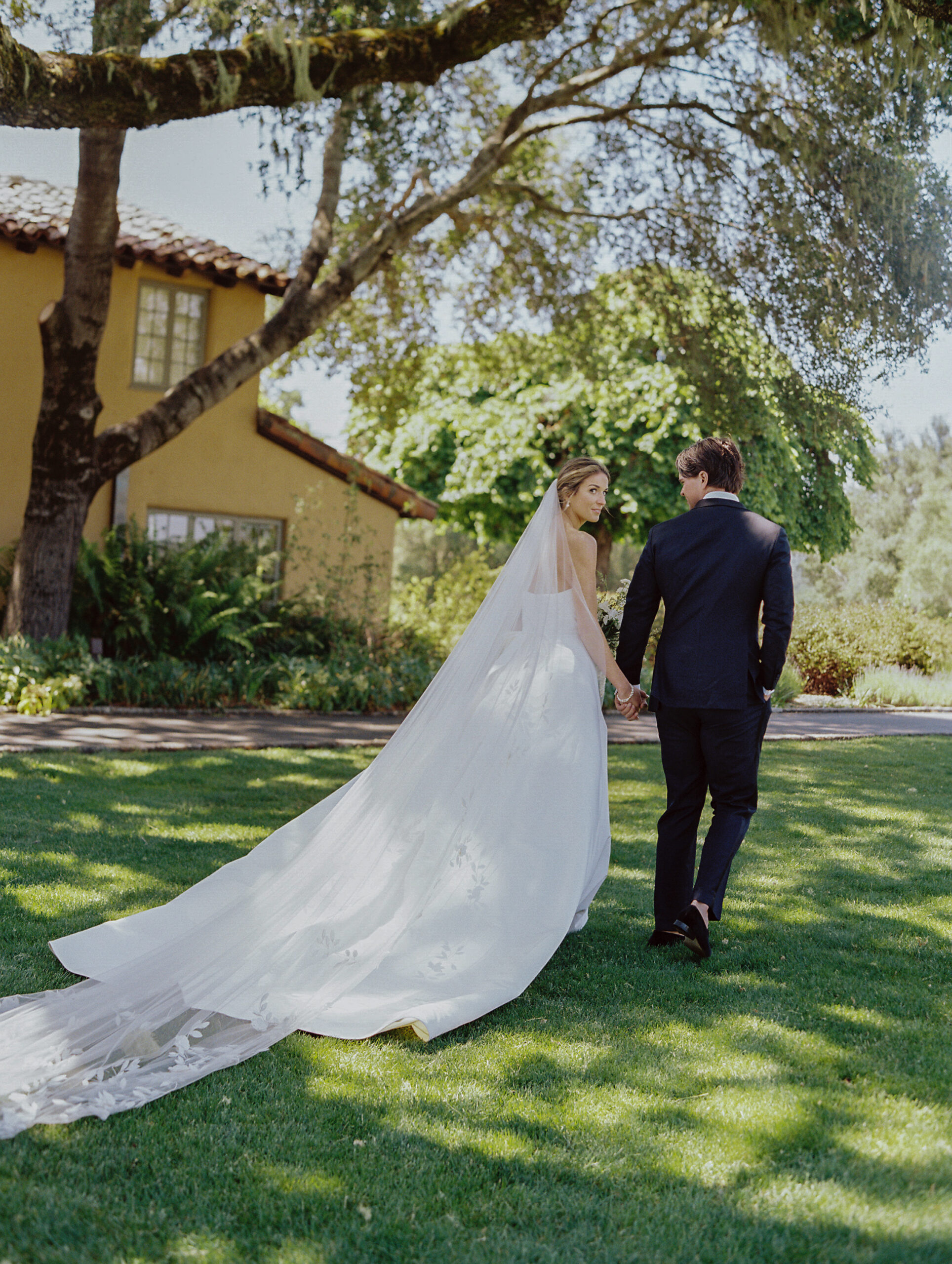 bride and groom walking hand in hand in front a the hacienda at the Santa Lucia preserve during their couple portraits.