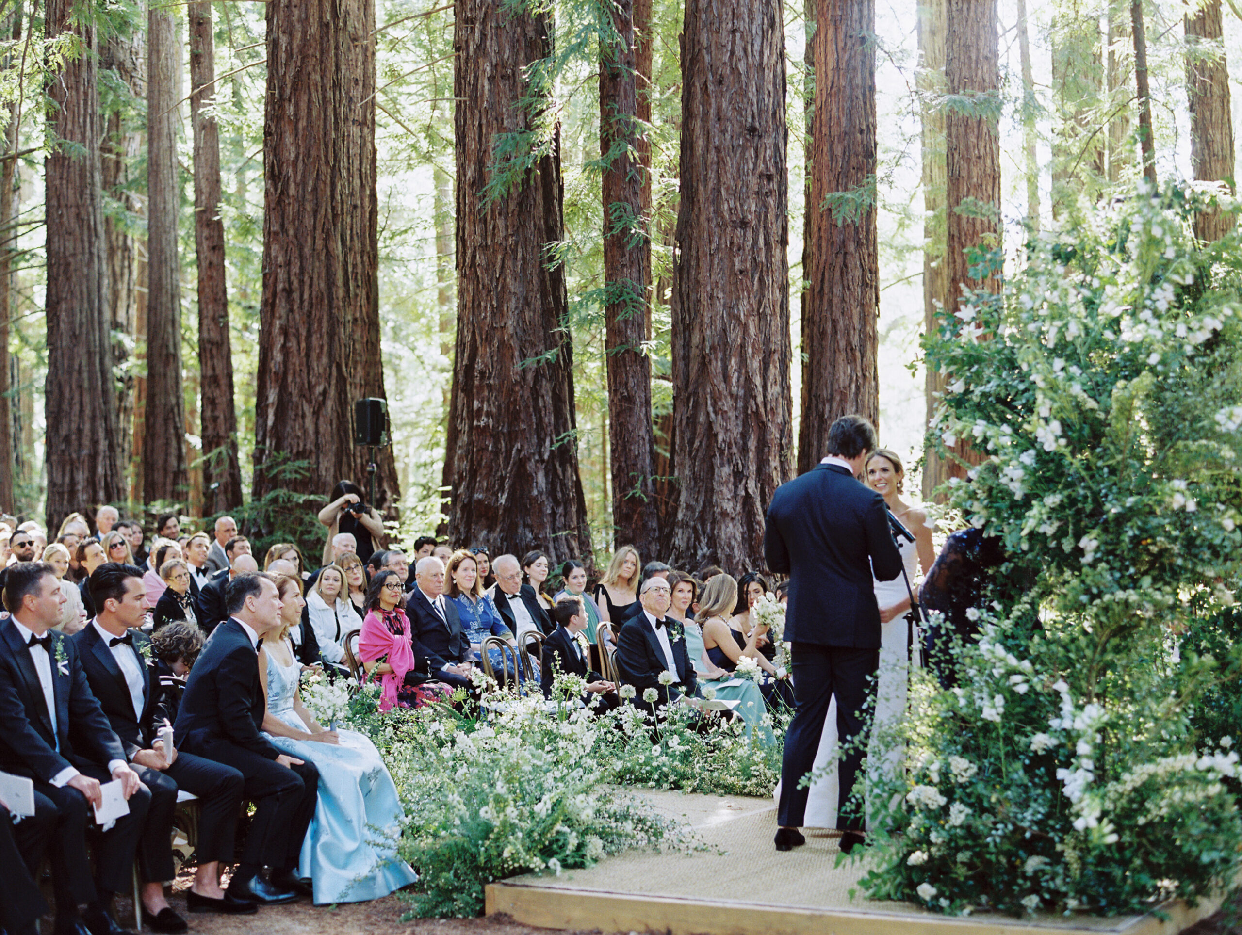 couple under a lush green and white ceremony arch at the redwood grove of Santa Lucia preserve.