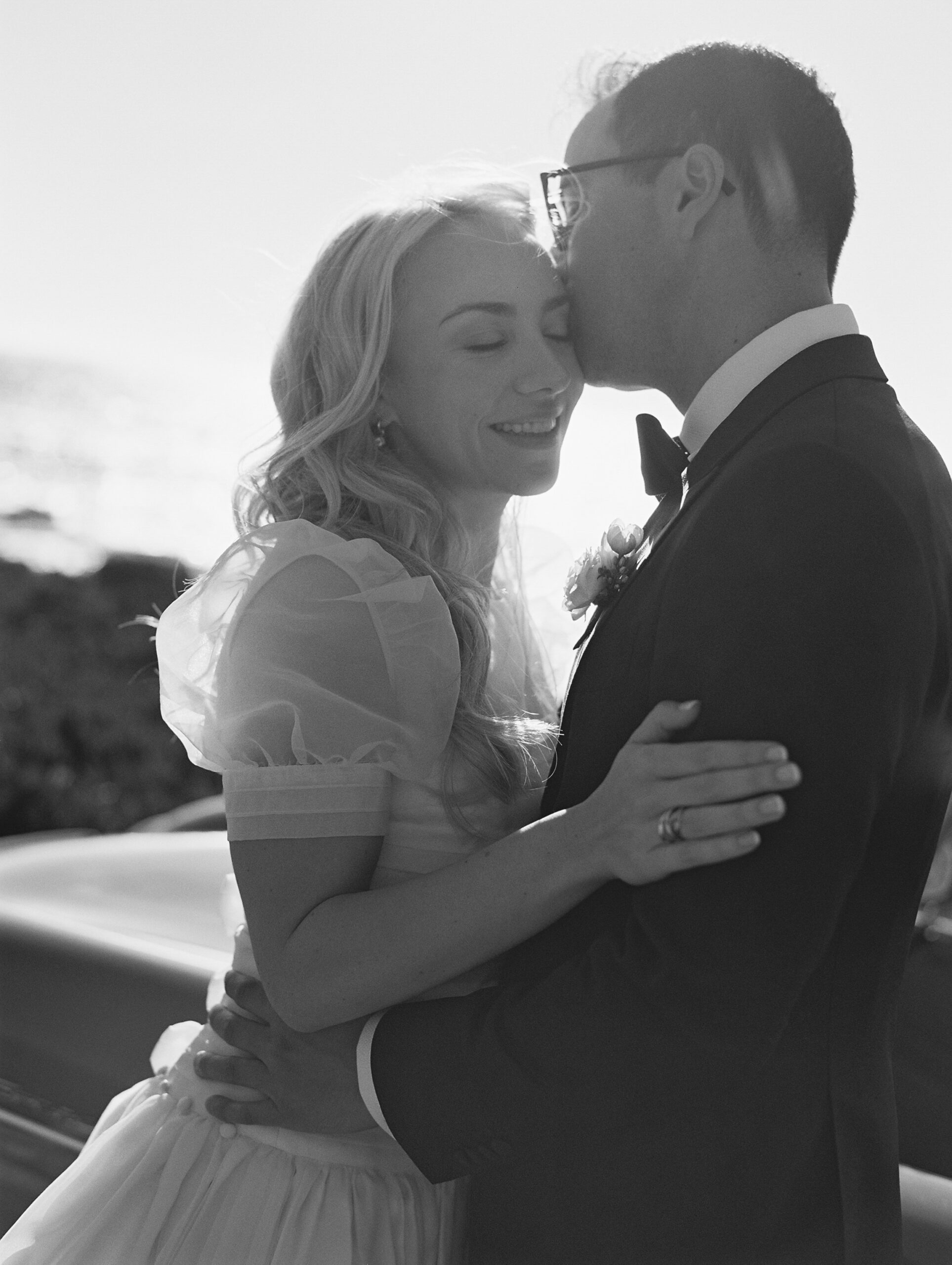black and white photo of couple cuddling with the sun behind them 