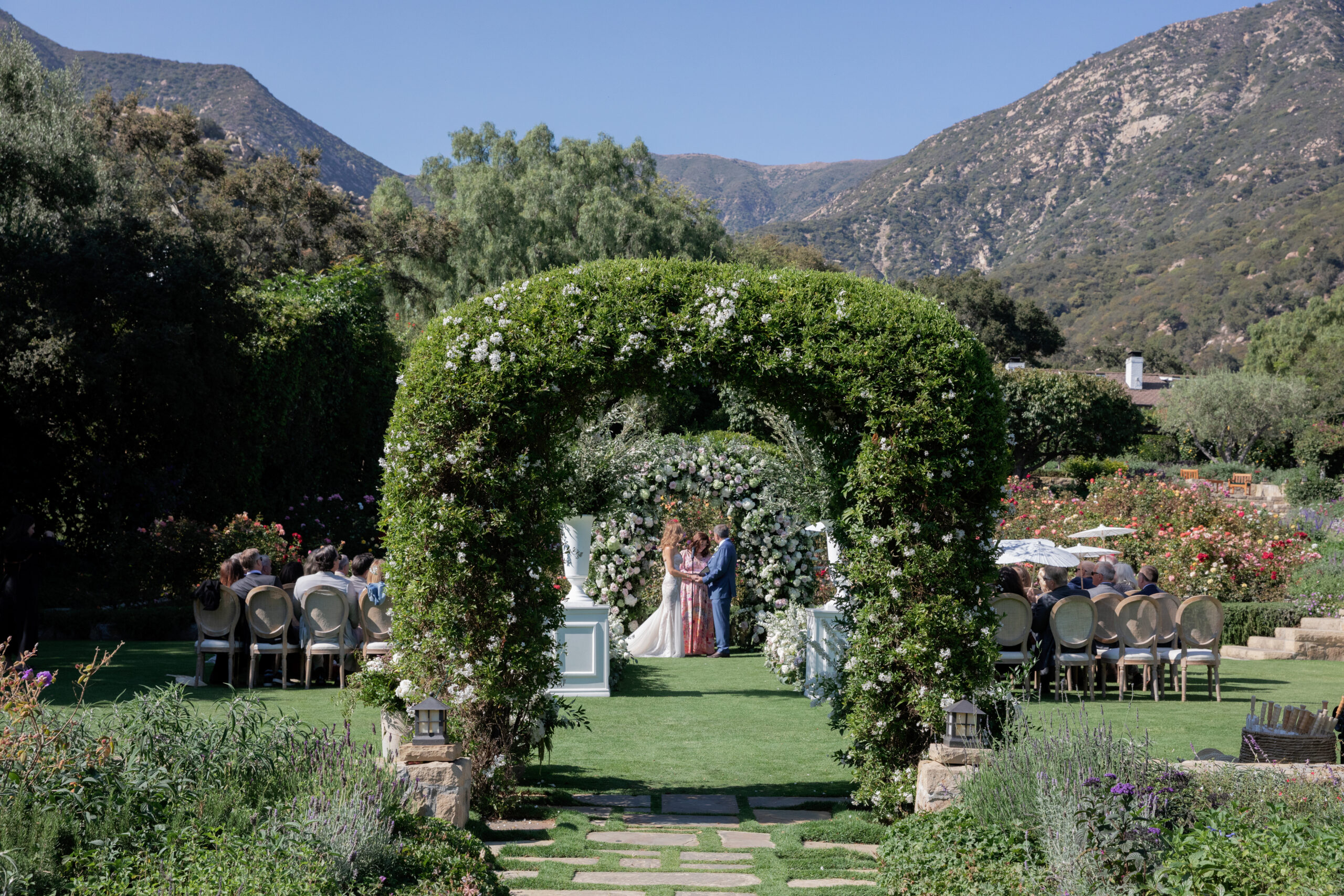 ceremony of a summer wedding with bride and groom under two arch ways. 